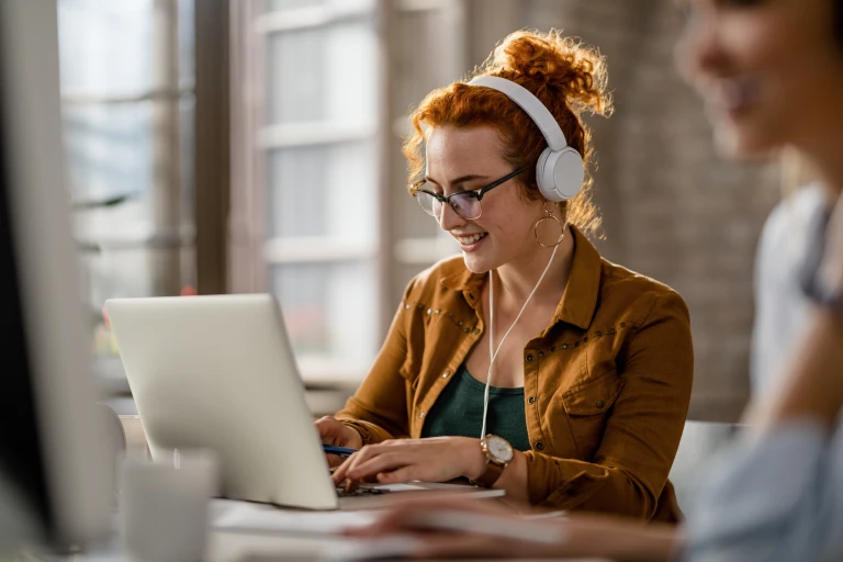 smiling creative businesswoman listening music headphones while working computer office